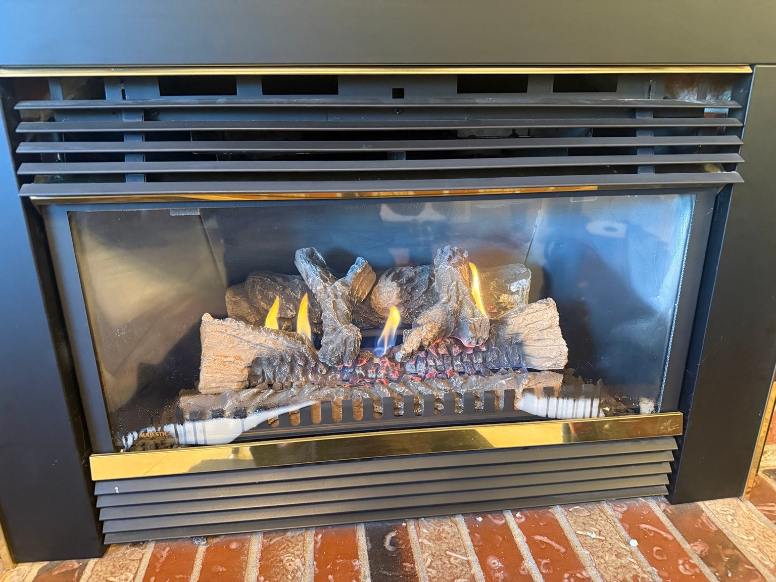 Gas fireplace with a black and brass front, decorative logs and lit flames
