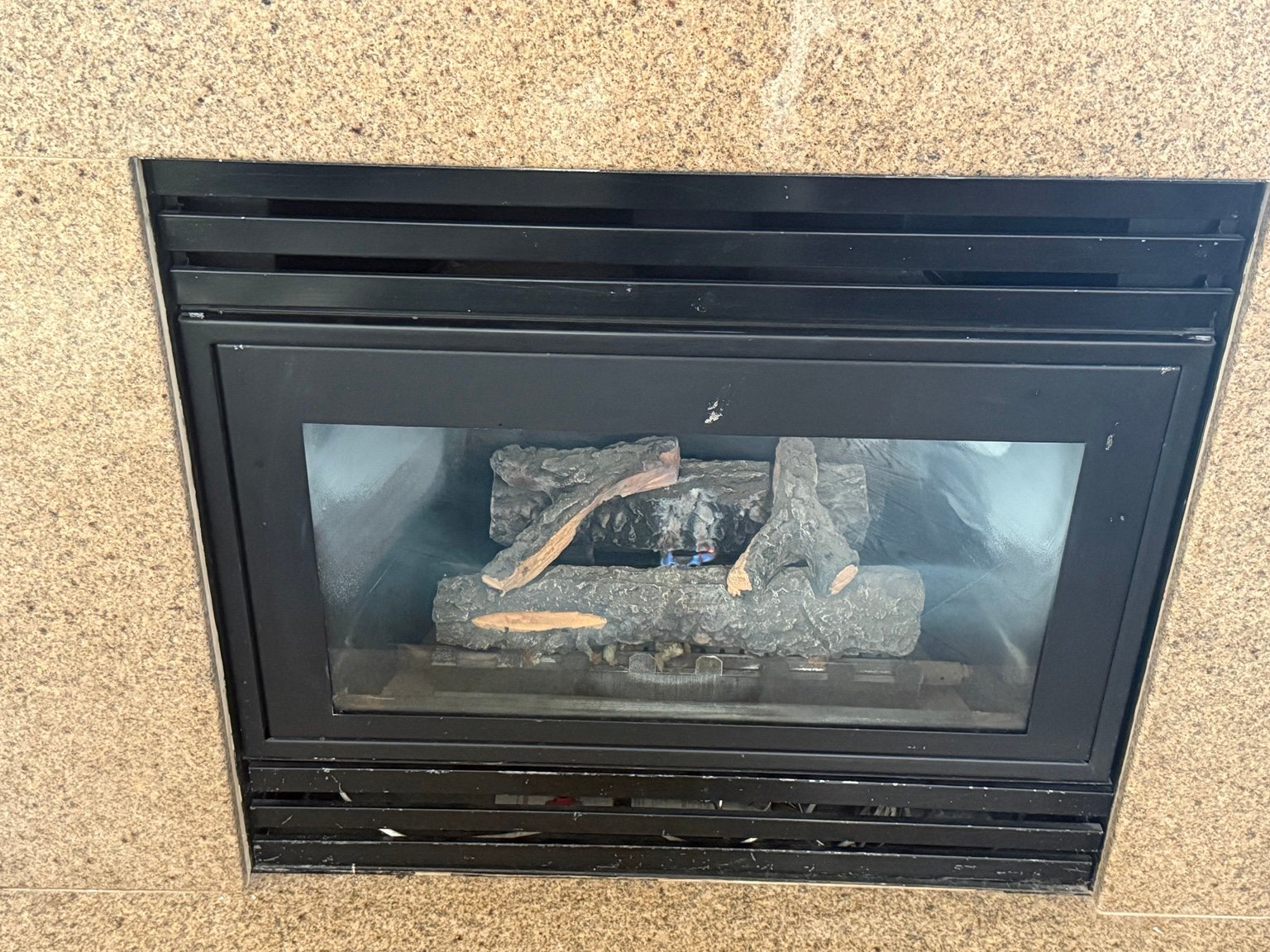 Gas fireplace with logs and a small visible flame in a brown tile surround